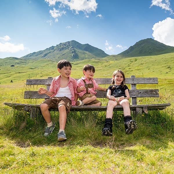 Kinder sitzen auf einer Holzbank in einer Berglandschaft